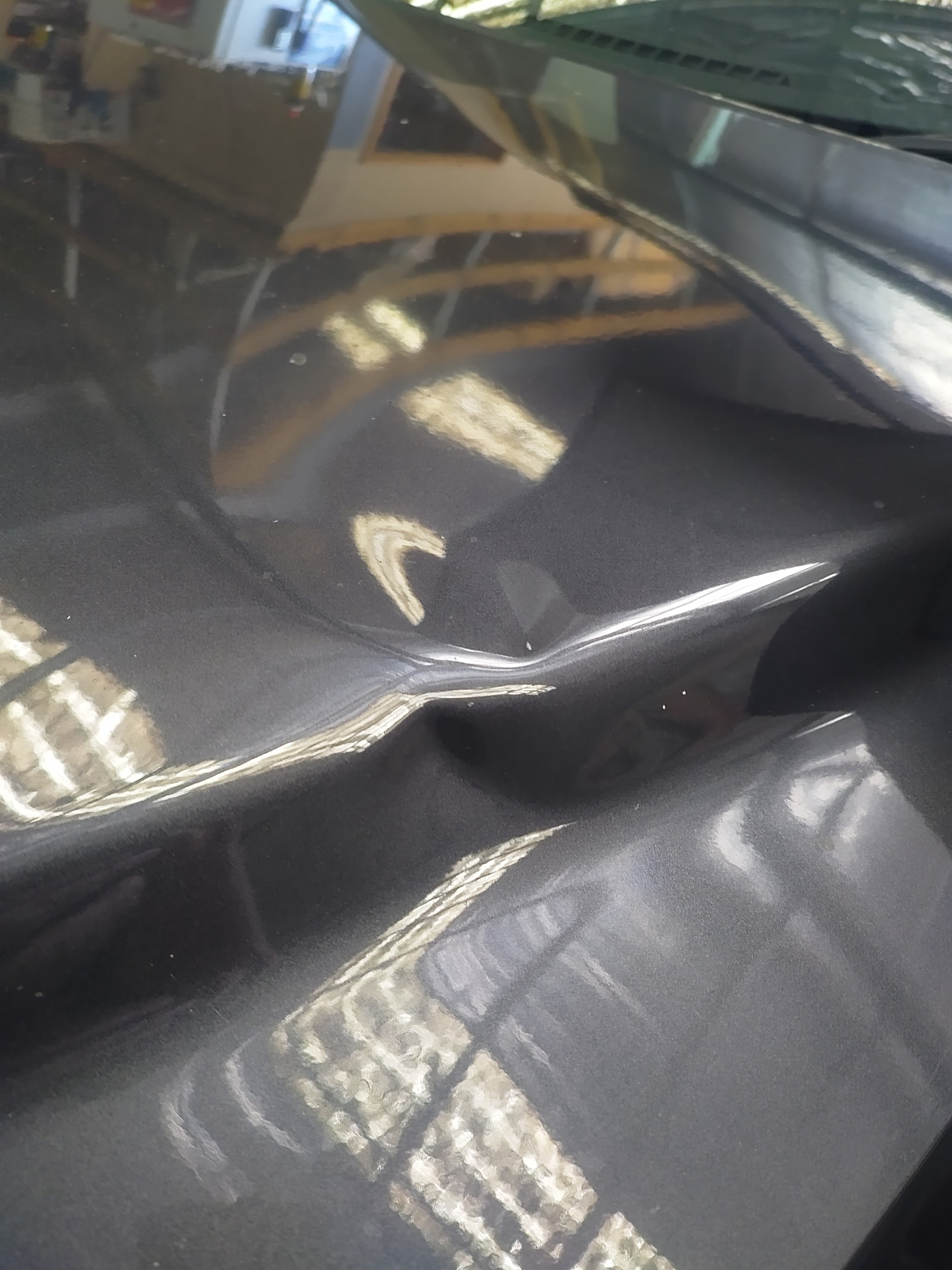 A long crease dent across the bonnet of a dark grey car, lit to show the damage