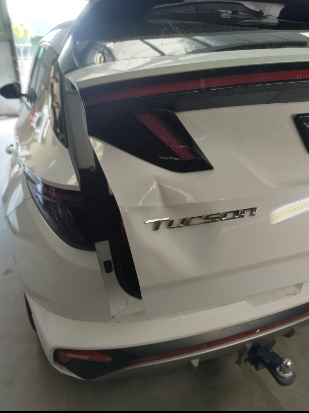 White Hyundai Tucson tailgate with a clear dent creasing the panel above the badge