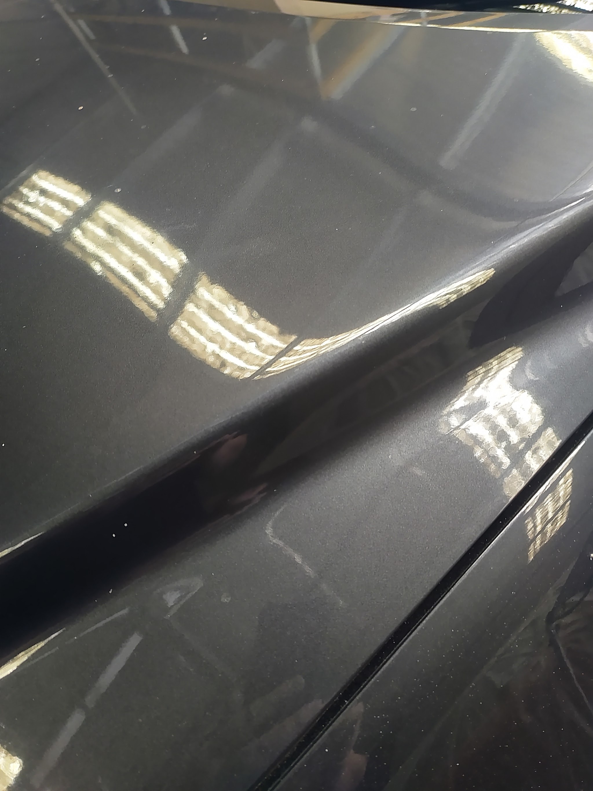 A crease sitting along a sharp body line on a dark metallic panel